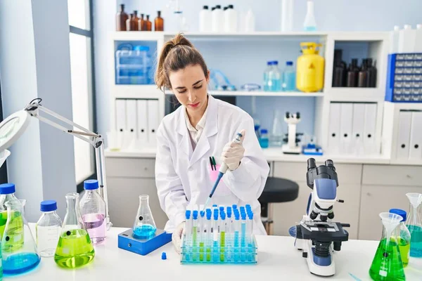 Laboratuvarda çalışan pipet kullanan bilim adamı üniforması giyen genç bir kadın.