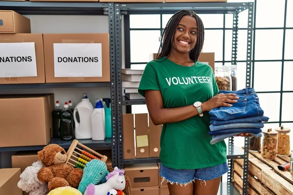 Young African American Woman Wearing Volunteer Uniform Holding Folded Jeans — Foto de Stock