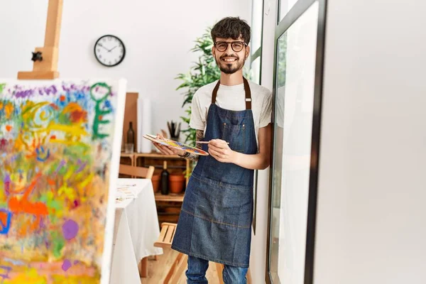 Genç İspanyol ressam mutlu bir şekilde resim stüdyosunda duruyor..