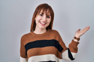 İzole edilmiş arka planda çizgili süveter giyen genç ve güzel bir kadın. Gülümseyen, mutlu bir sunum yapan ve avuç içi kameraya bakan.. 