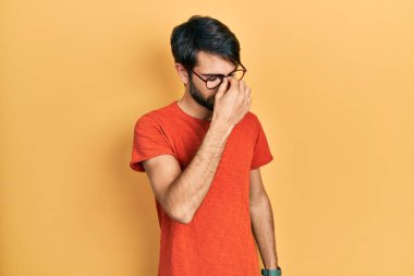 Gündelik kıyafetler ve gözlük takan genç İspanyol adam yorgun burnu ve gözleri ovuşturup yorgunluk ve baş ağrısı hissediyor. Stres ve hüsran kavramı. 