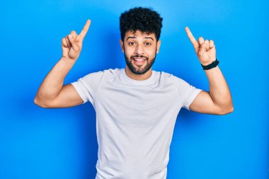 Sakallı, sıradan beyaz tişörtlü genç bir Arap. Şaşırmış, şaşırmış, parmaklarıyla işaret ediyor ve kollarını kaldırıyordu.. 