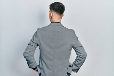 Kulakları genişlemiş, iş ceketi giymiş, kolları vücutta geriye doğru bakan beyaz bir çocuk. 