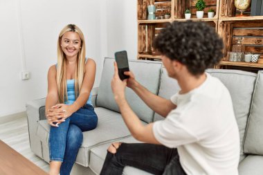 Genç adam evde akıllı telefon kullanarak kız arkadaşının resmini çekiyor.