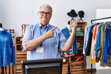 Gri saçlı yaşlı adam perakende mağazasında yönetici olarak çalışıyor. Gülümsüyor ve kameraya bakıyor. İki eliyle ve parmaklarıyla onu işaret ediyor.. 
