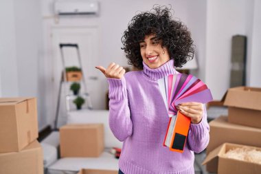 Kıvırcık saçlı, yeni ev duvarının rengini seçen genç esmer kadın baş parmağını yana kaldırıyor ve ağzı açık gülümsüyor. 
