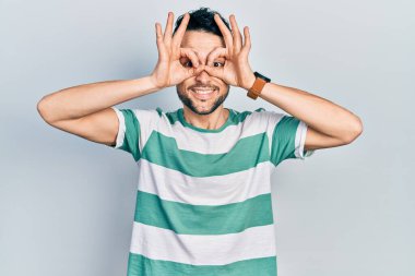 Günlük kıyafetler giyen genç İspanyol adam dürbün gibi jest yapıyor. Dürbün dilini çıkarıyor, gözler parmaklarından bakıyor. çılgın ifade. 