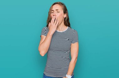 Gündelik kıyafetler giyen genç sarışın kadın ağzıyla ağzını kapatmaktan sıkılmış. Huzursuz ve uykulu.. 