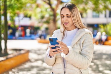 Parkta akıllı telefon kullanan kendine güvenen genç bir kadın.