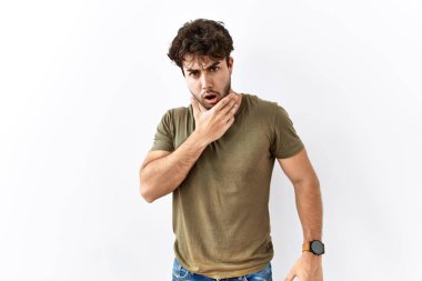 Hispanic man standing over isolated white background looking fascinated with disbelief, surprise and amazed expression with hands on chin 