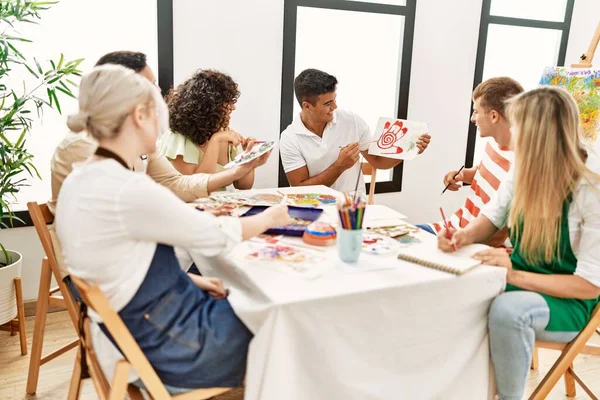 Group of people smiling happy drawing sitting on the table at art studio.