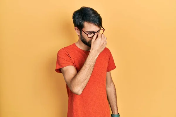 カジュアルな服や眼鏡を着て若いヒスパニック系の男は 鼻や目をこすり疲れや頭痛を感じて疲れている ストレスとフラストレーションの概念 — ストック写真