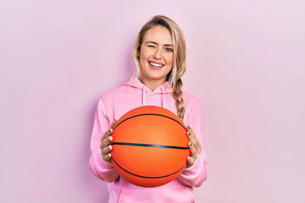 Hermosa Joven Rubia Sosteniendo Bola Baloncesto Guiñando Ojo Mirando Cámara —  Fotos de Stock