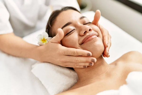 Young latin woman relaxed having face massage at beauty center