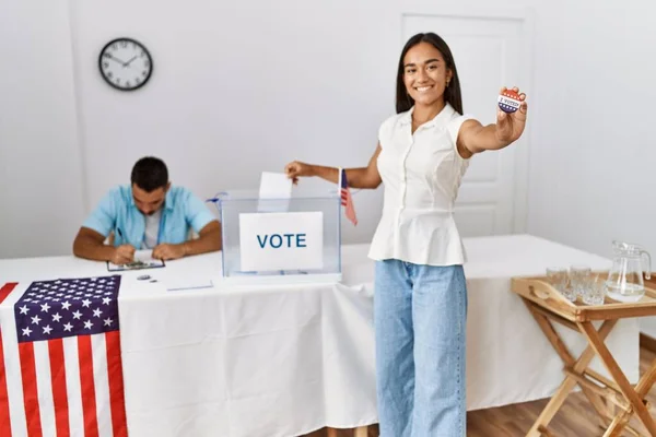 Young american voter woman holding badge and putting vote in ballot box at electoral college.