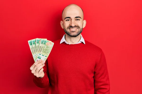 Młody Łysy Mężczyzna Trzymający Argentyńskie Peso Banknoty Wyglądające Pozytywnie Szczęśliwie — Zdjęcie stockowe