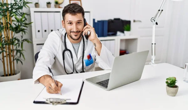 Young Hispanic Man Wearing Doctor Uniform Talking Smartphone Clinic — Foto de Stock