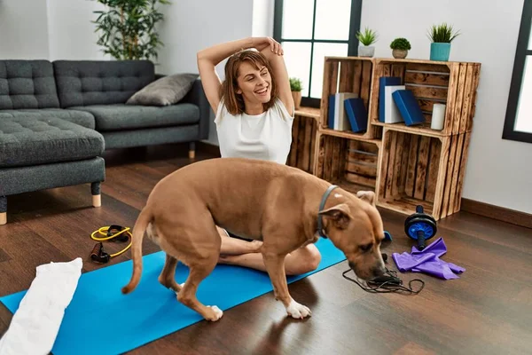 Young caucasian woman smiling confident stretching with dog at home