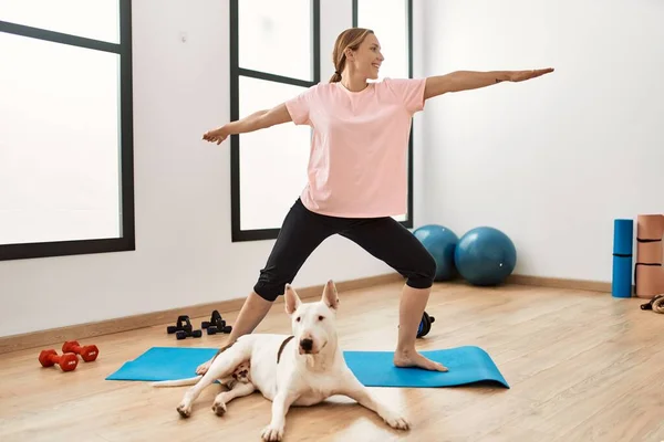 Young caucasian woman smiling confident training yoga with dog at sport center