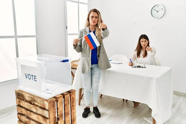 Young blonde woman at political stand holding russia flag pointing with finger to the camera and to you, confident gesture looking serious