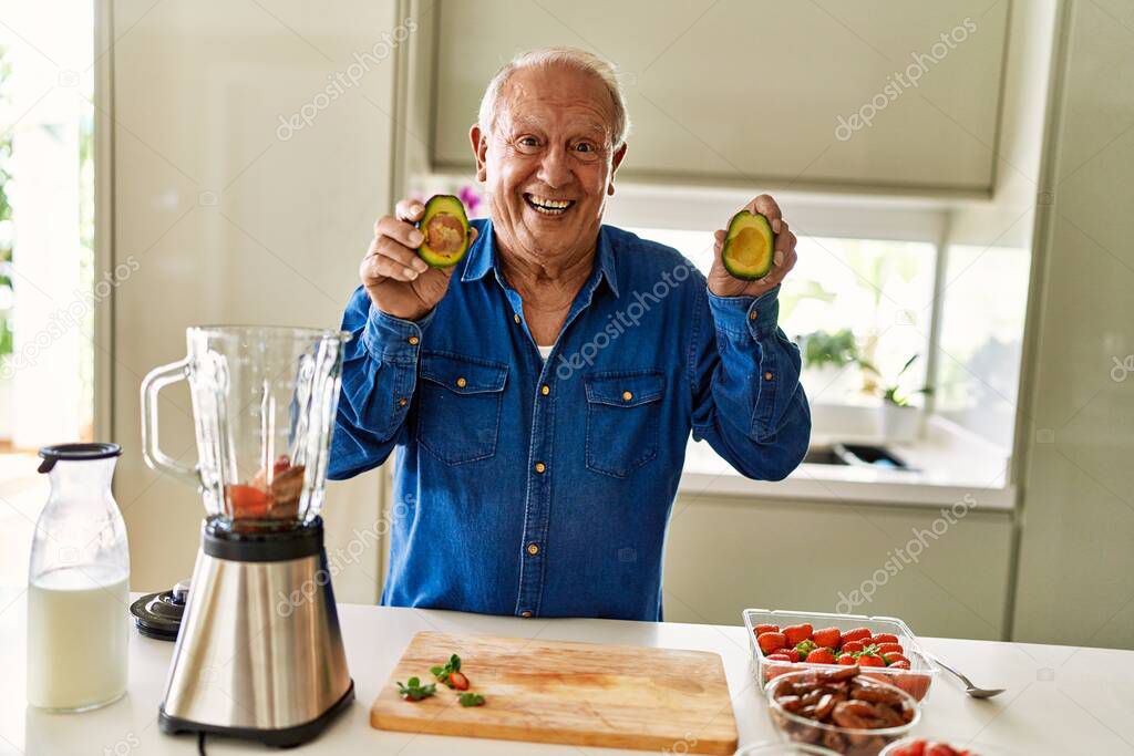 Senior man smiling confident holding two middles avocado at kitchen