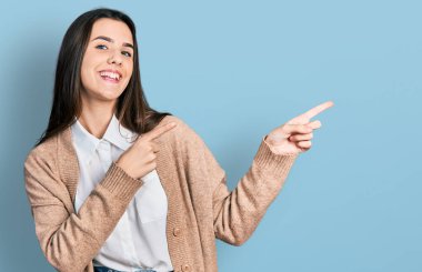 Young brunette teenager wearing casual white shirt and jacket smiling and looking at the camera pointing with two hands and fingers to the side. 
