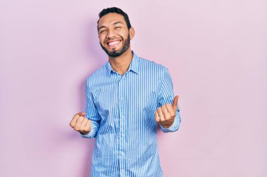 Mavi gömlekli İspanyol bir adam mutlu ve heyecanlı bir şekilde kolları havada, gülümseyen ve başarı için bağıran bir jest yapıyor. kutlama konsepti. 