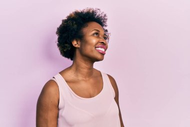 Genç Afro-Amerikalı kadın kolsuz tişört giyiyor. Yüzünde gülümseme, doğal bir ifade ile yan yana bakıyor. Kendinden emin gülen. 