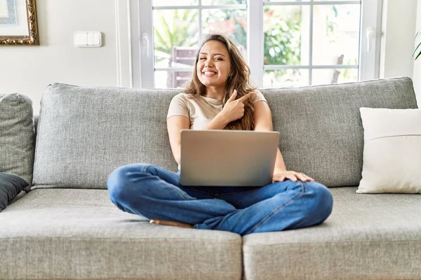 Güzel, genç, esmer bir kadın evinde bilgisayar laptopuyla oturuyor. Yüzünde mutlu ve doğal bir ifadeyle, elleri ve parmaklarıyla gülümsüyor. 