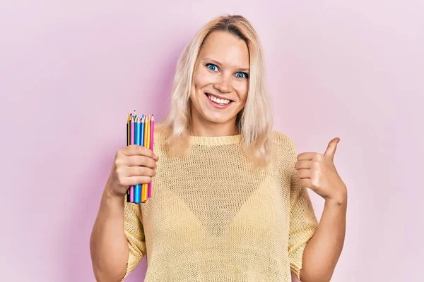 Piękne Biały Blondynka Kobieta Trzyma Kolorowe Ołówki Wskazując Kciuk Górę — Zdjęcie stockowe