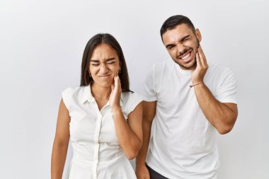 Irklar arası genç çift, izole edilmiş arka planda bir arada durup diş ağrısı ya da diş ağrısı yüzünden ağızlarına acı dolu bir ifadeyle dokunuyor. dişçi 