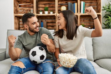 Genç latin çift evde futbol maçı izleyip porpcorn yiyorlar..