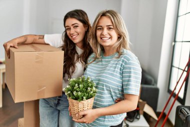 Mutlu bir şekilde gülümseyen genç bir çift yeni evine karton kutu ve saksı yerleştiriyor..