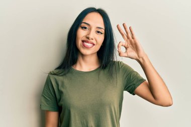 Gündelik tişört giyen genç İspanyol kız olumlu gülümsüyor ve el ve parmaklarıyla 