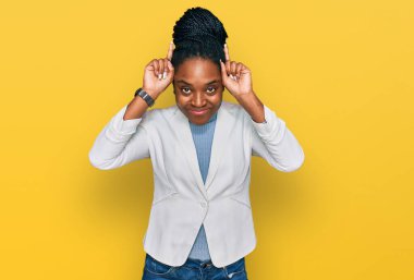 Genç Afro-Amerikan kadın iş kıyafetleri içinde parmaklarıyla boynuz gibi komik hareketler yapıyor. 