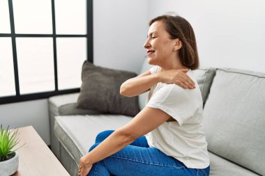 Orta yaşlı İspanyol bir kadın evinde boynu ağrıyan bir kanepede oturuyor.