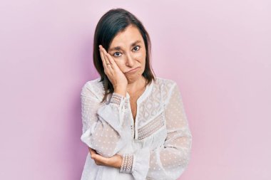 Orta yaşlı İspanyol bir kadın günlük kıyafetler giyip kollarını kavuşturarak depresyondan sıkılmış ve yorgun görünüyor.. 