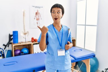 Kısa saçlı, İspanyol bir kadın ağrı kesici kliniğinde çalışıyor. El parmağı yana dönük, ağzı açık, şaşkın bir ifadeyle şaşırdı.. 