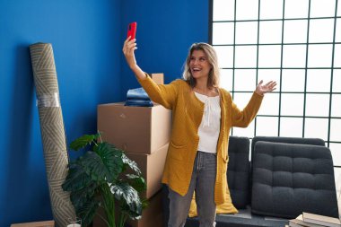 Genç sarışın kadın kendine güvenen yeni evinde akıllı telefonun yanında özçekim yapıyor.