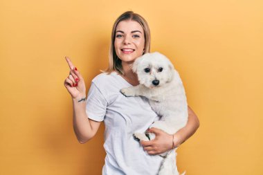Güzel, beyaz bir kadın sevimli bir köpeğe sarılıyor, gülümsüyor mutlu bir şekilde elini ve parmağını yana uzatıyordu. 