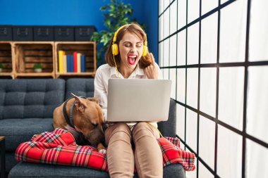 Genç ve güzel bir kadın dizüstü bilgisayar kullanıyor. Kanepede oturuyor, gülümsüyor. 