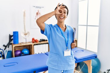 Kısa saçlı, İspanyol bir kadın. Ağrı giderme kliniğinde çalışıyor. El hareketleriyle gülümsüyor.. 