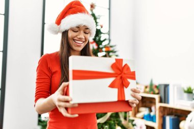 Genç Latin kadın boks hediyesini açıyor. Noel ağacının yanında duruyor.
