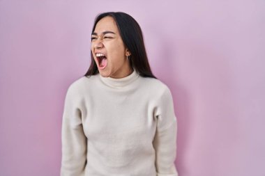 Pembe arka planda duran genç Güney Asyalı kadın kızgın ve kızgın çığlık atıyor ve öfkeliydi, öfkeyle bağırıyordu. öfke ve agresif konsept. 