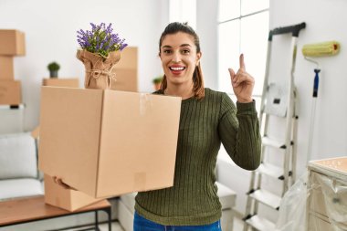 Young hispanic woman holding cardboard box at moving surprised with an idea or question pointing finger with happy face, number one 
