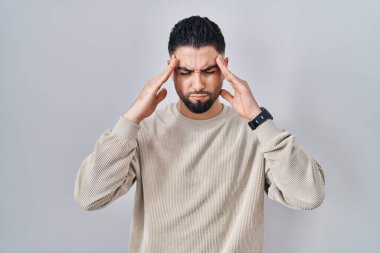 Tecrit edilmiş arka planda duran yakışıklı genç bir adam, elleri başının üstünde, stres yüzünden başı ağrıyor. migren ağrısı. 