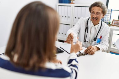 Doktor üniforması giyen orta yaşlı bir adam ve kadın klinikte tıbbi danışmanlık yapıyorlar.