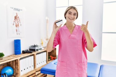 Ağrı kesici kliniğinde çalışan genç fizyoterapist kadının elinde mutlu ve olumlu gülümseyen bir kredi kartı var. 