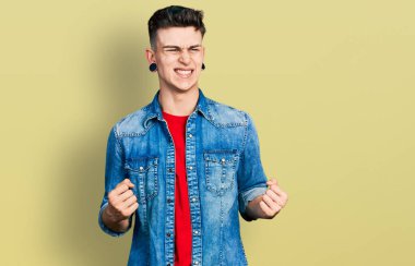 Kulakları genişlemiş, sıradan bir kot ceket giymiş kolları havada ve gözleri kapalı zaferi kutlayan genç beyaz bir çocuk. Kazanan konsept. 