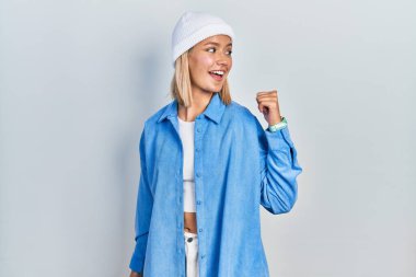 Güzel sarışın kadın, yün şapka takıyor, gülümsüyor, gülümsüyor ve başparmağıyla yan tarafa bakıyor.. 